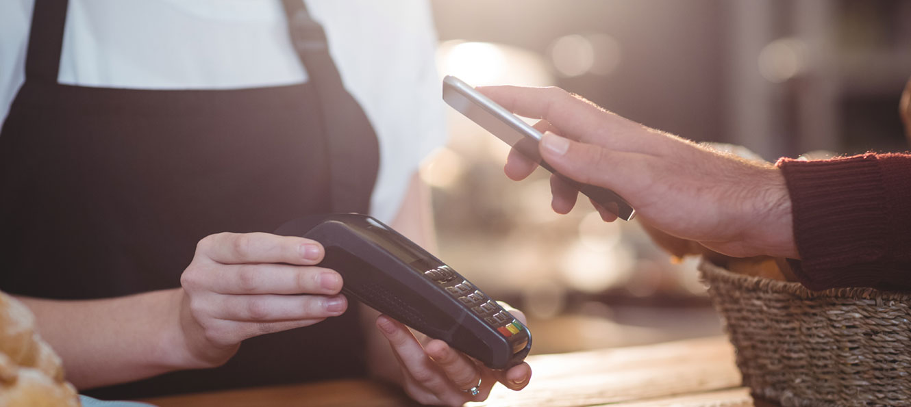 hand holding smartphone over a payment terminal to pay with their digital wallet app