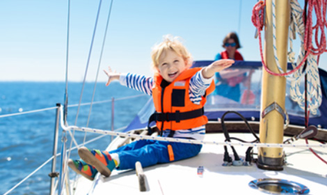 young child smiling and wearing a bright orange safety vest on the deck of a boat